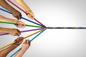 Multiple diverse people twist colorful ropes together into one unified multicolor rope